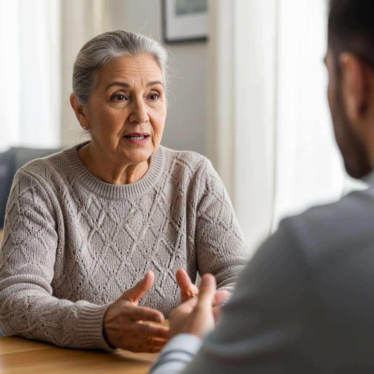 Older woman seated across from a younger adult in a calm living room conversation, waist-up centered view