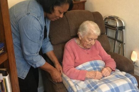 A middle-aged woman adjusting a protective pad on a recliner where an elderly woman is seated