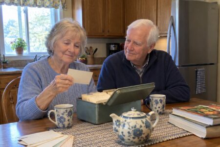 Older couple sitting at a table going through a box of handwritten recipe cards