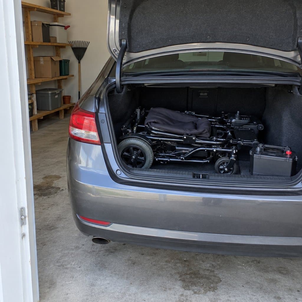 Folded power wheelchair lying in the open trunk of a car in a garage